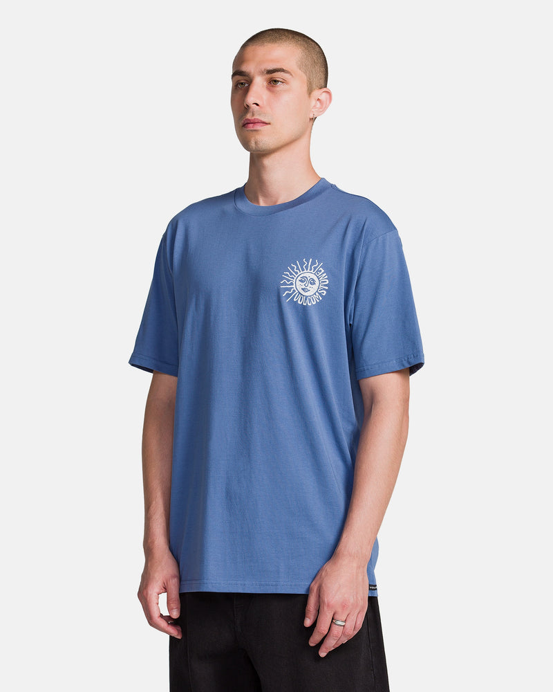 A person wears the Volcom Men's Mazatlan Short Sleeve Tee, featuring a white sun and smiling face graphic on the upper left chest, standing against a plain white background.