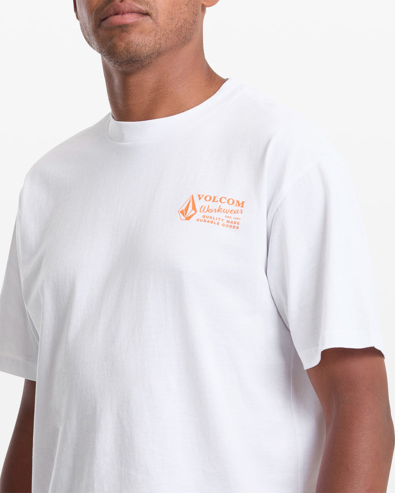 A man wears a Volcom Men's Workwear Short Sleeve Tee in white, featuring an orange Durable Goods logo on the left chest, standing against a white background.