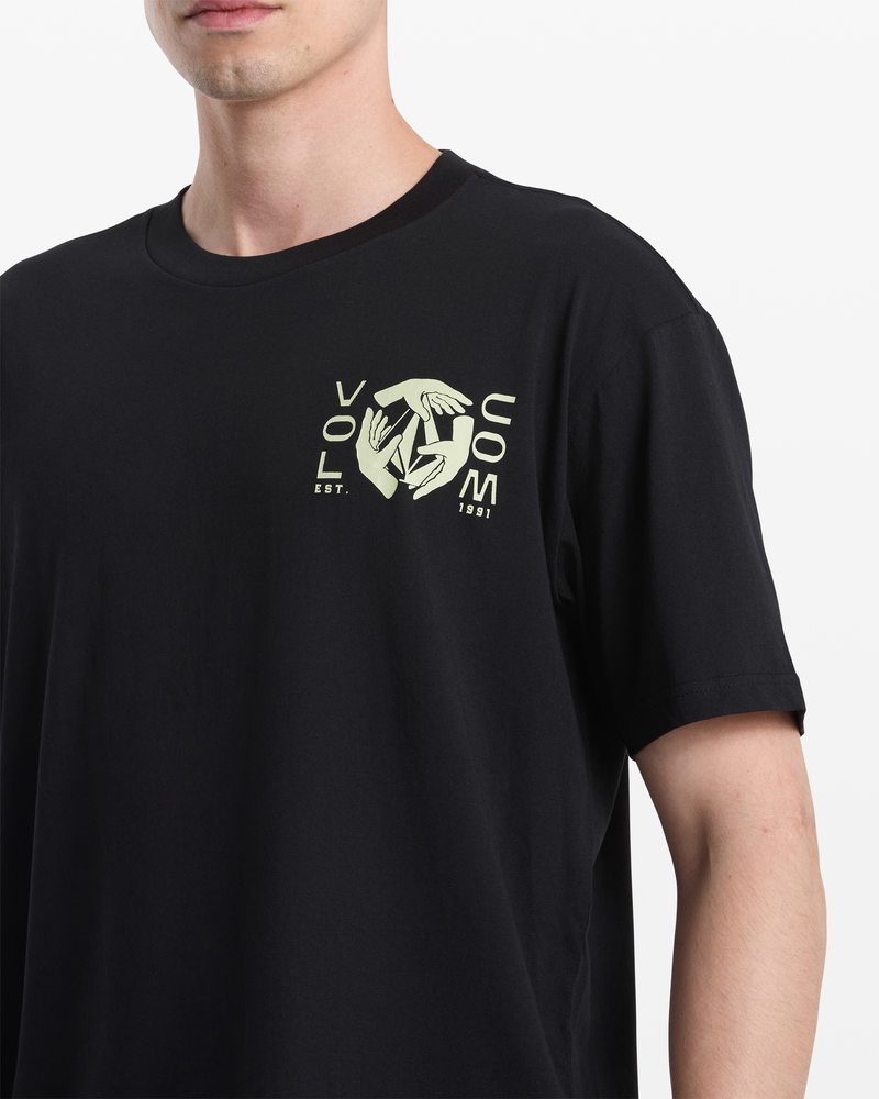 A person wears the Volcom Men's Handeling Short Sleeve Shirt, a black 100% cotton slim tee with illustrated hands and “VOLCOM EST. 1991.” The Outdoor Earth Tripper’s face is partially out of frame.