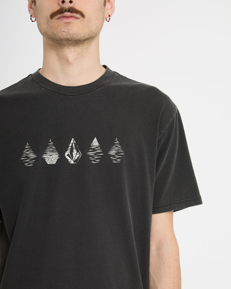A man with a mustache and earrings wears the Volcom Men's Lunar Phases Short Sleeve Tee, featuring geometric tree and diamond graphics on black, photographed against a plain white background.