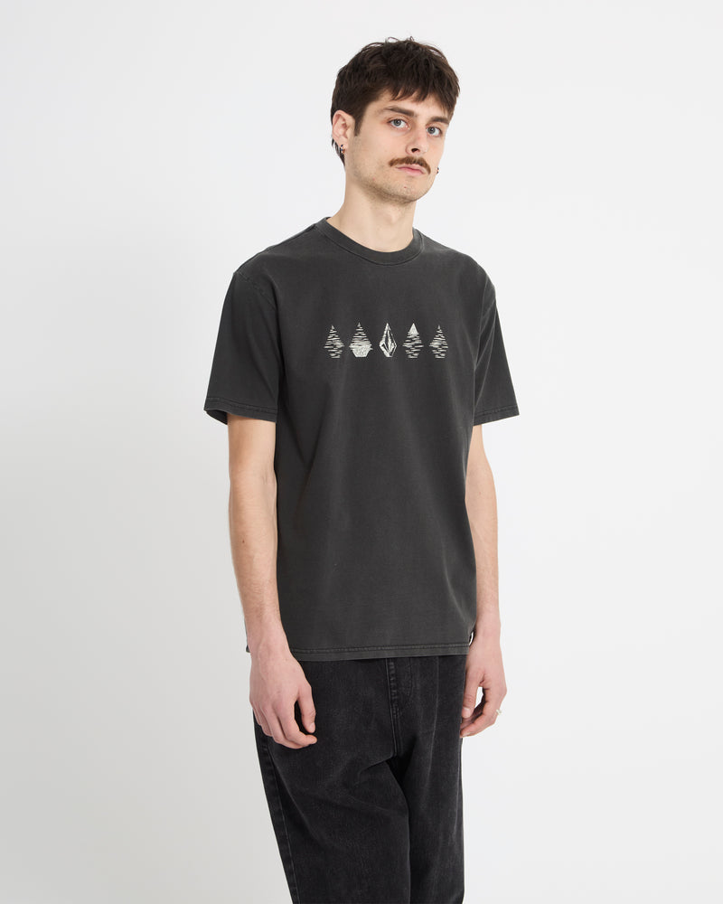 A young man with short dark hair and a mustache wears a Volcom Men's Lunar Phases Short Sleeve Tee and black jeans, standing against a plain white background.