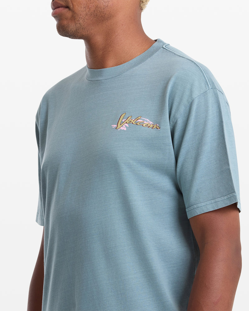 A man in the Volcom Men's Zorch Short Sleeve Tee—light blue, 190gm cotton, with a small colorful logo on the left chest—stands against a plain white background.