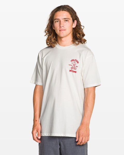 A young man with long wavy hair wears the Volcom Men's Temptations Short Sleeve Tee in soft cotton, featuring a small red graphic and text on the left chest, paired with gray shorts, standing against a plain white background.