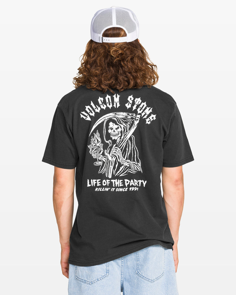 A person with long hair, wearing a white mesh cap and the Volcom Men's Eternal Short Sleeve Tee in black with a soft-hand reaper graphic, plus light blue shorts, is seen from behind against a plain backdrop.