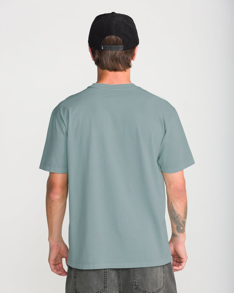 Back view of a person wearing a sage green loose fit Volcom Men’s Ransom Stitch Short Sleeve Tee and a black baseball cap.