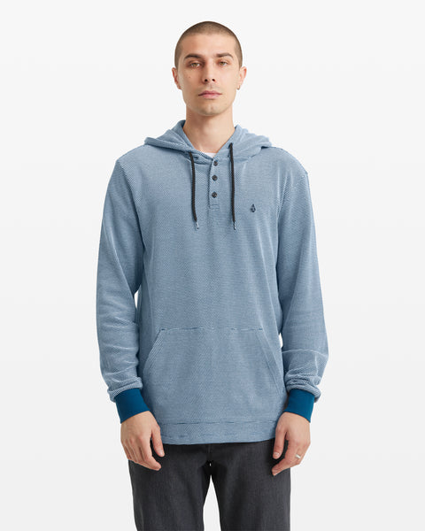 A man with short hair wears a light blue Volcom Men's Murph Thermal Long Sleeve hoodie, featuring a Henley placket, slub waffle knit, dark blue drawstrings and cuffs. He stands facing forward with hands relaxed at his sides against a white background.