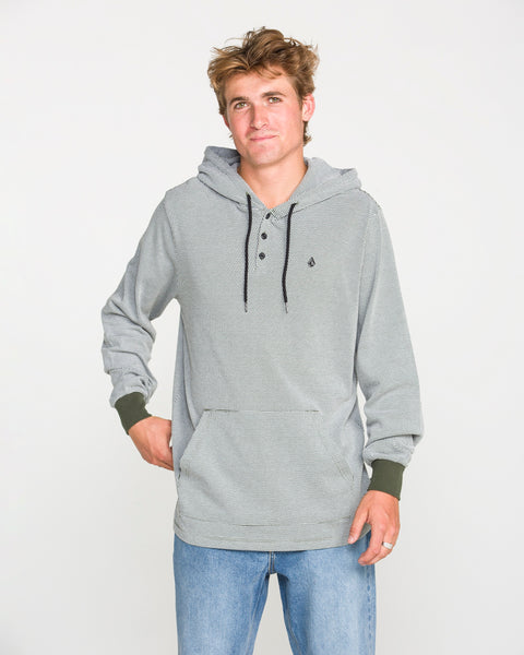 A young man wearing the Volcom Men's Rowan Thermal Long Sleeve Shirt in light gray, featuring black drawstrings, pairs it with blue jeans as he stands against a plain white background, looking at the camera with a relaxed expression.