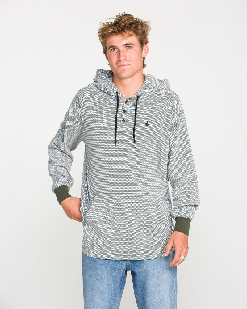 A young man wearing the Volcom Men's Rowan Thermal Long Sleeve Shirt in light gray, featuring black drawstrings, pairs it with blue jeans as he stands against a plain white background, looking at the camera with a relaxed expression.