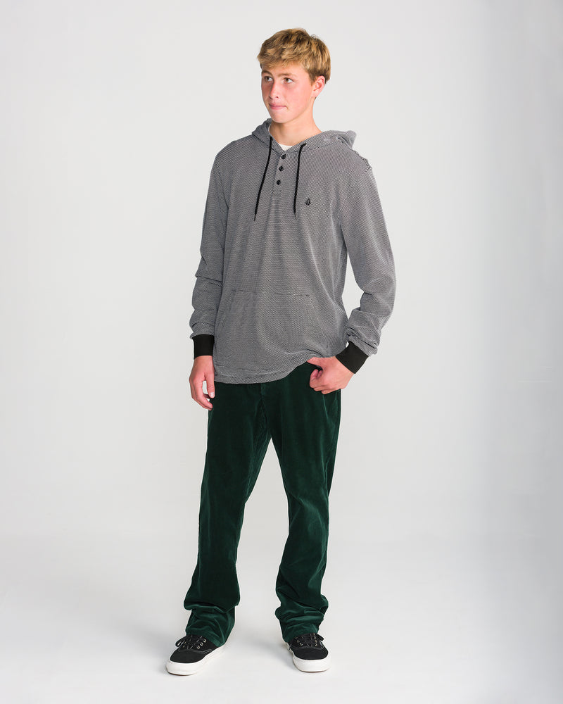 A young man wearing a Volcom Men’s Rowan Thermal Long Sleeve in a black and white popcorn knit, paired with dark green pants and black sneakers.