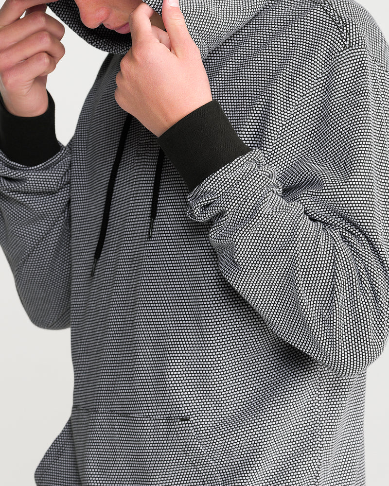 A person pulling up the hood of a Men’s Rowan Thermal Long Sleeve, featuring a small-scale, two-tone popcorn knit texture and black cuffs.