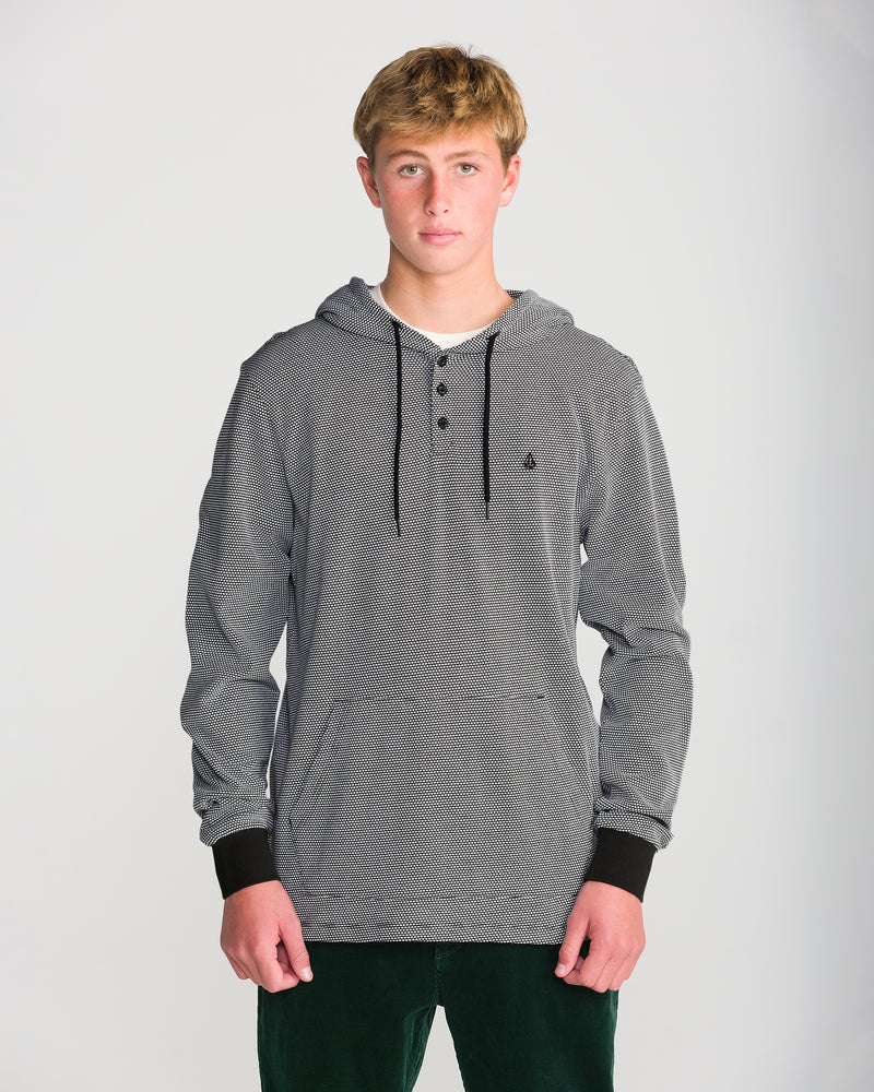A young man wears a Volcom Men’s Rowan Thermal Long Sleeve, a black and white popcorn knit thermal henley with a hooded three-button placket and black cuffs.
