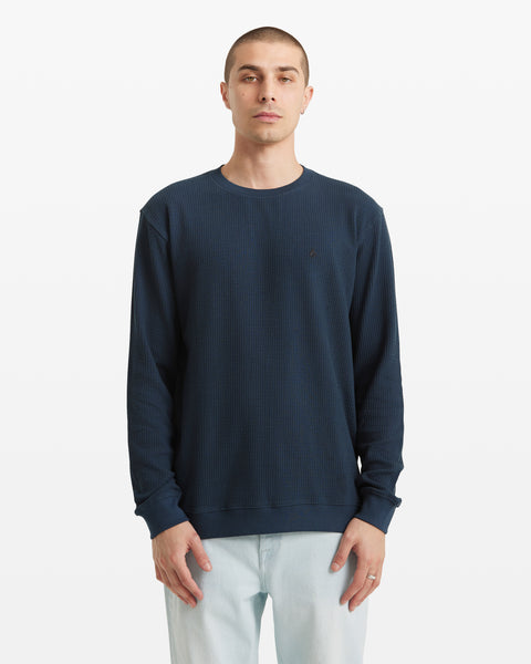 A person with short hair faces forward, wearing the Volcom Men's Gridstone Crew Long Sleeve in dark blue and light-colored pants, set against a plain white background.