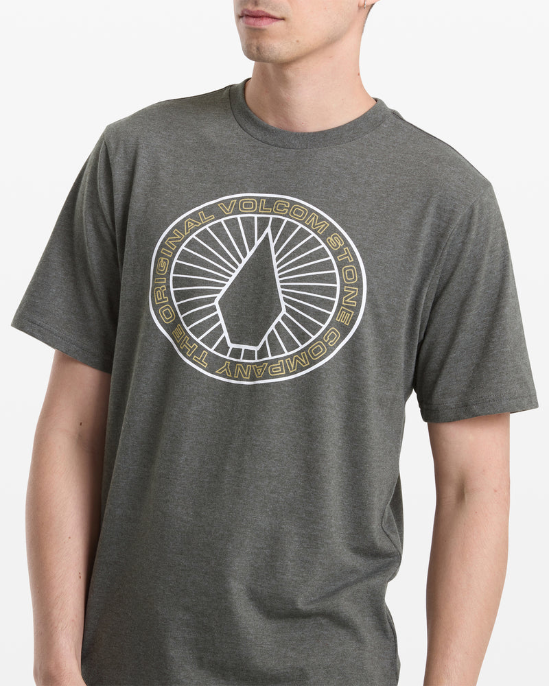 A person wears the Volcom Men's Medalist Short Sleeve Tee in Squadron Green heather, with the brand’s logo and “The Original Volcom Stone Company” in a circular print on the front.