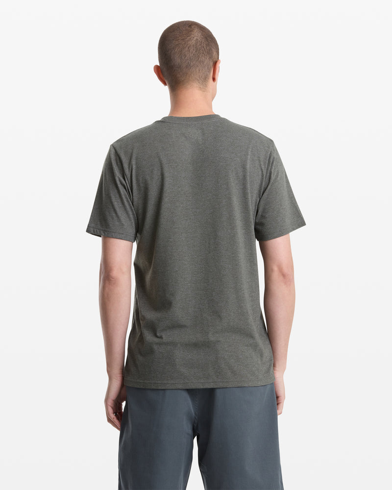A person with short hair stands with their back to the camera, wearing the Volcom Men's Medalist Short Sleeve Tee and gray shorts against a plain white background.