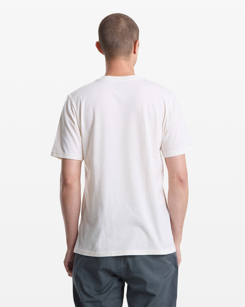 A person with short hair is shown from the back, wearing a Volcom Men's Giddy Up Short Sleeve Tee in white and gray pants, standing against a white background.