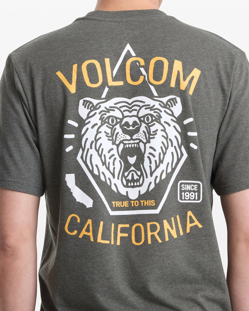 A man wears the Volcom Men's Golden Statement Short Sleeve Tee, featuring a roaring bear graphic, "VOLCOM CALIFORNIA," a small California state outline, "TRUE TO THIS," and "SINCE 1991" on the back.