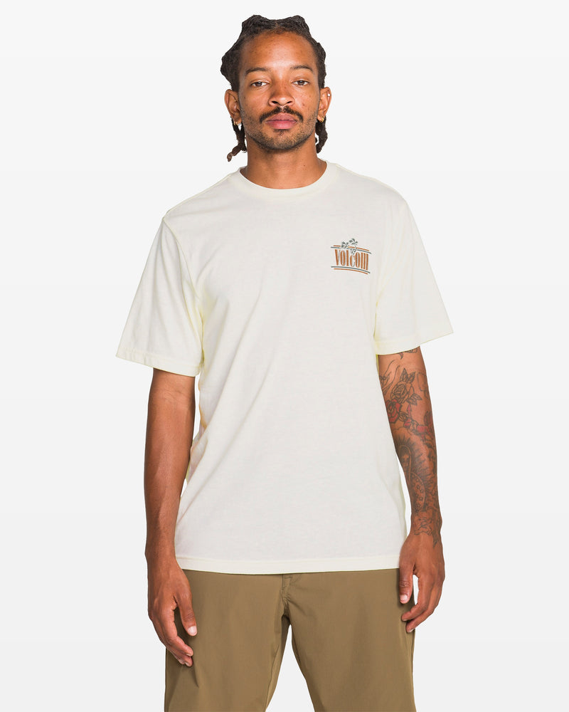 A person with dreadlocks and tattoos on their right arm wears the Volcom Men's Breathe Deep Short Sleeve Tee in heather, featuring a small left chest graphic, paired with khaki shorts, standing against a plain white background.