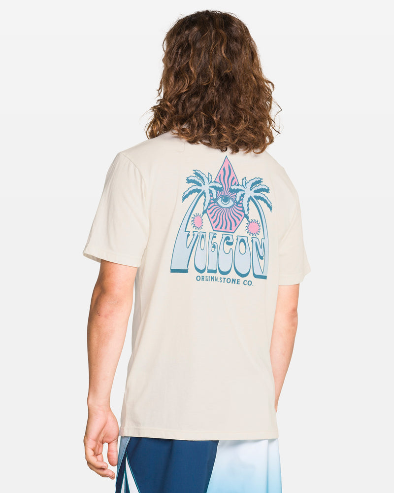 A person with long, wavy brown hair wears the Volcom Men's All Seeing Short Sleeve Tee in Off White Heather, featuring a colorful palm tree and triangle eye graphic. The modern fit tee pairs perfectly with blue and white shorts.
