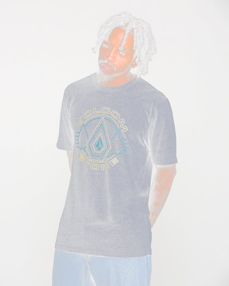 A person with light-colored, curly hair wears a gray Volcom Men's Line Feld Short Sleeve Tee and blue jeans, standing against a plain white background.