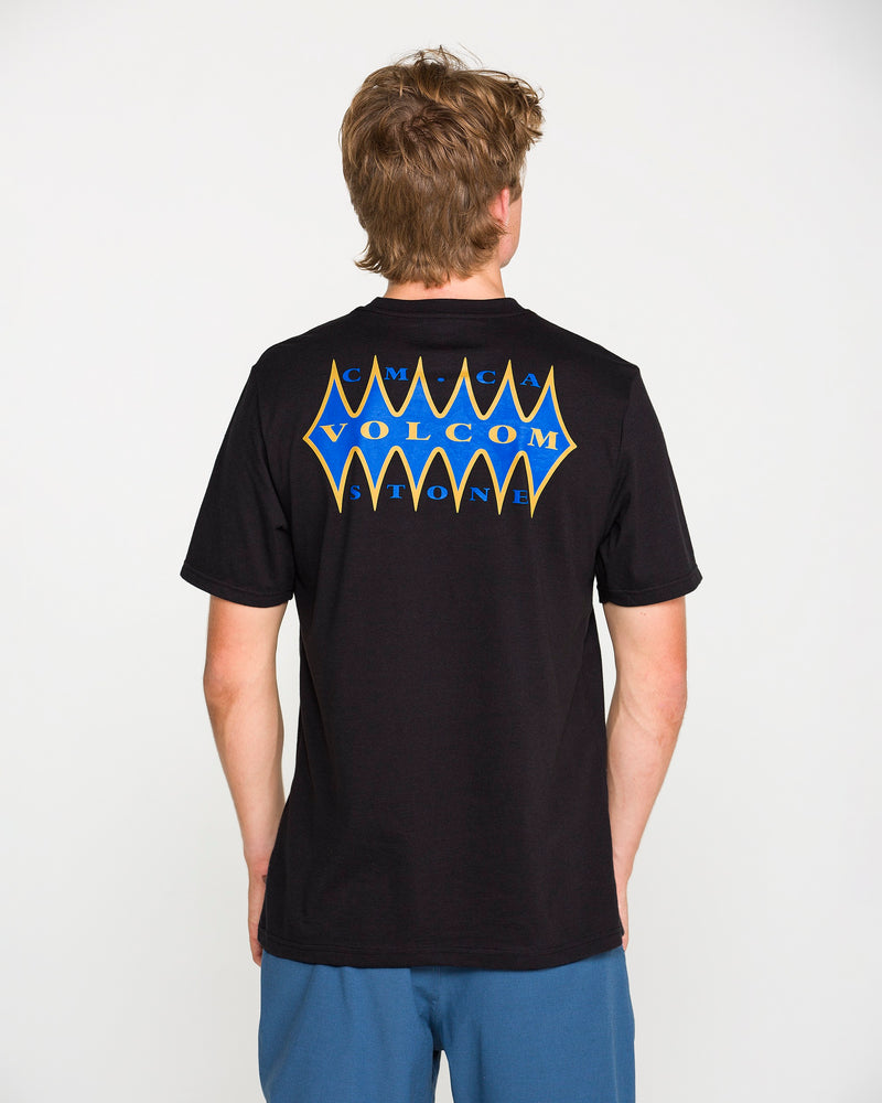 A person with short brown hair, wearing the Volcom Men's Smokers Lounge Short Sleeve Tee in washed black heather—with a blue and yellow Volcom Stone graphic on the back—stands facing away from the camera.