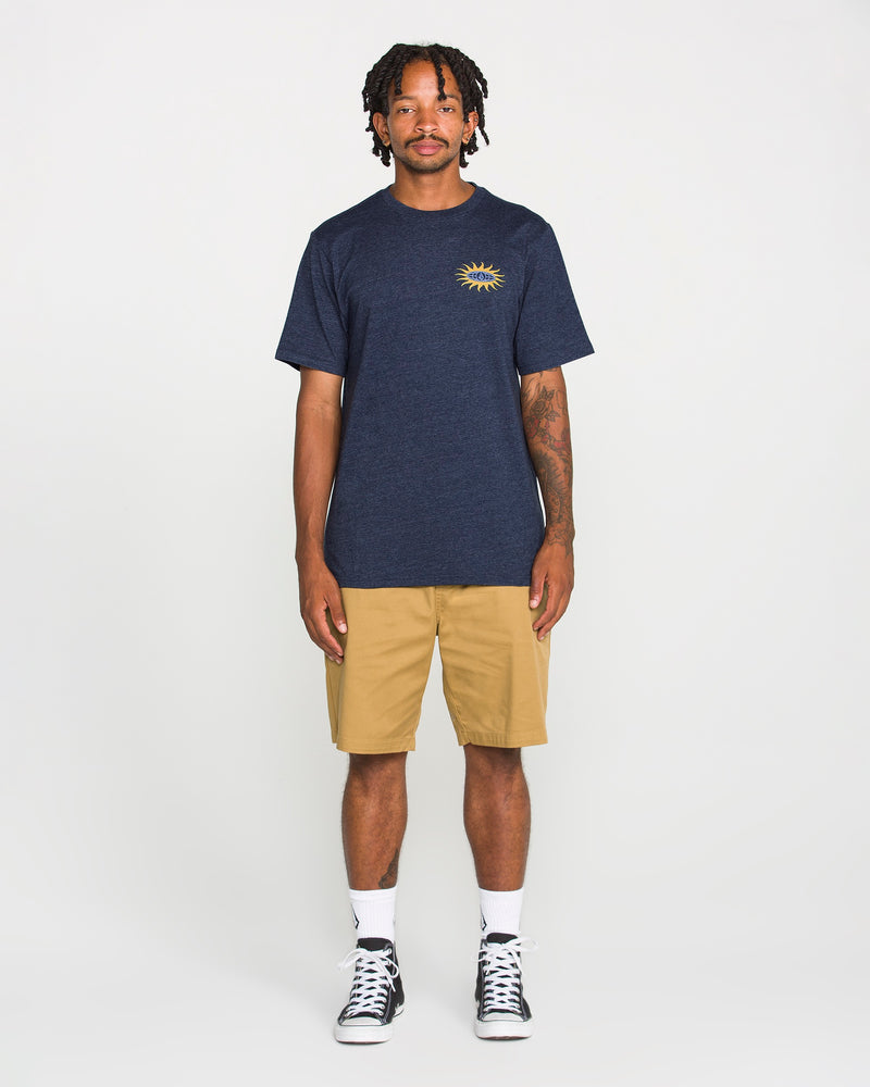 A person stands facing forward, wearing a Volcom Men's Spf91 Short Sleeve Tee in navy with a sun graphic on the chest, paired with khaki shorts, white socks, and black high-top sneakers. The background is plain white.