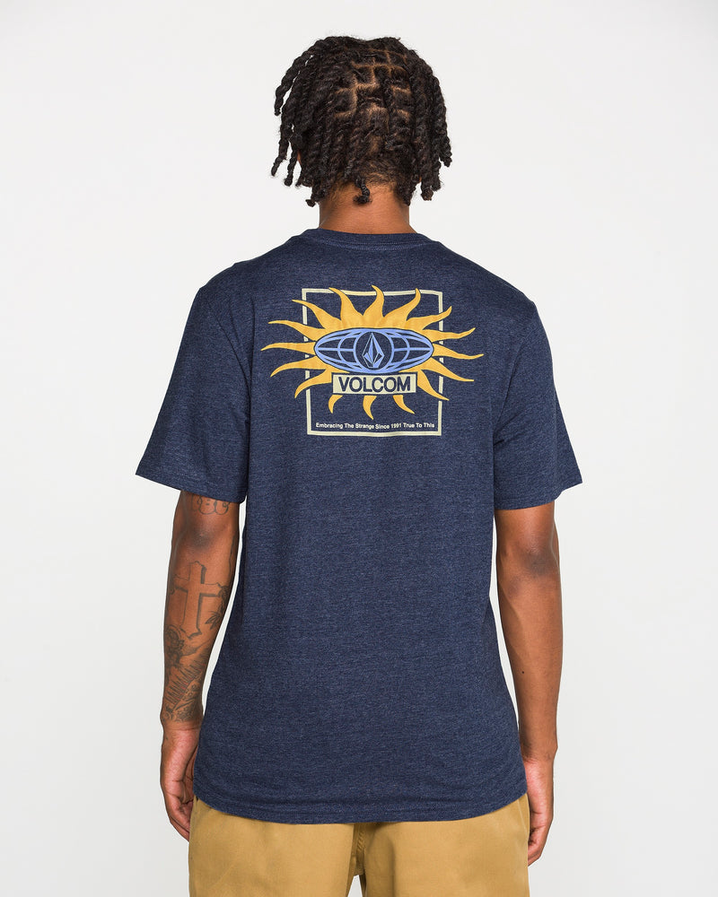 A person faces away, wearing the Volcom Men's Spf91 Short Sleeve Tee in navy blue, featuring a sun graphic and logo on the back. The medium-weight heather tee is paired with tan shorts, standing out against a plain white background.