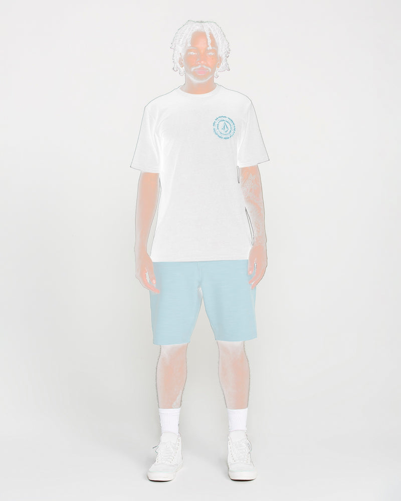 A man with light dreadlocks, dressed in the Volcom Men's Still Spiraling Short Sleeve Tee styled with light blue shorts and white sneakers, stands against a plain white background. His image appears partially faded and outlined.