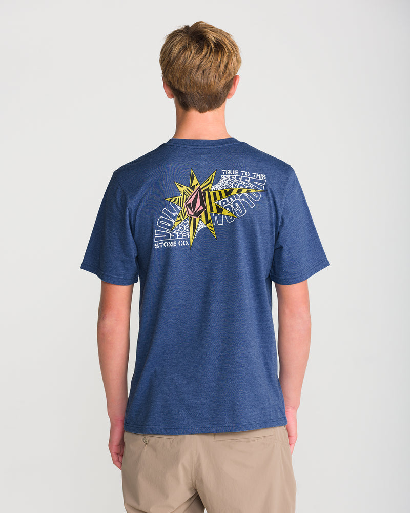 A person with short blond hair wears the Volcom Men’s Op Blast Short Sleeve Tee in blue, showing its colorful compass graphic and text on the back. The ring-spun cotton shirt is viewed from behind on a white background.