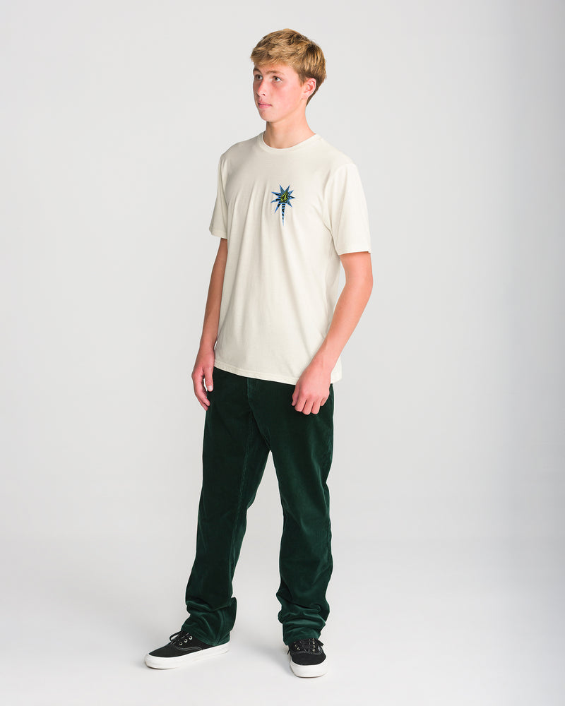 A man wearing a cream-colored Men’s Op Blast Short Sleeve Tee with a star-shaped graphic on the chest, paired with dark green pants and black sneakers.