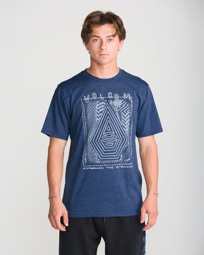 A young man wears the Volcom Men’s Insomniac Short Sleeve Tee, a modern fit heathered tee with geometric patterns and text, standing against a plain light background and looking at the camera with a neutral expression.