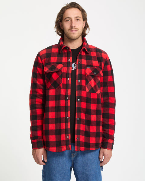 A man stands facing forward against a white background, wearing the Volcom Men's Bowered Fleece Long Sleeve in red and black plaid over a black t-shirt and blue jeans.