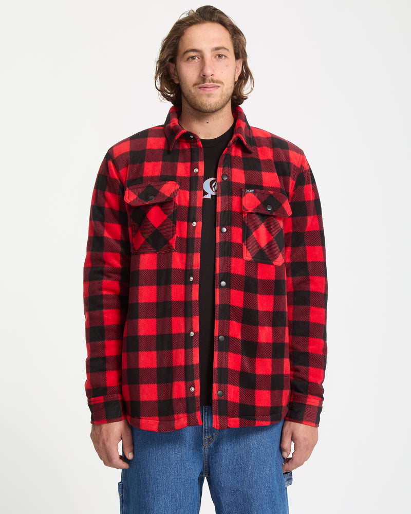 A man stands facing forward against a white background, wearing the Volcom Men's Bowered Fleece Long Sleeve in red and black plaid over a black t-shirt and blue jeans.