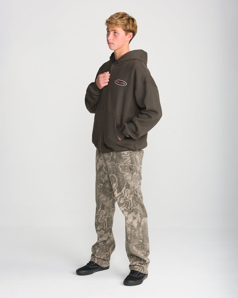 A person wearing a dark brown Volcom Men’s Driggs Workwear Zip hooded sweatshirt with an oval logo on the chest and patterned camouflage-style pants.