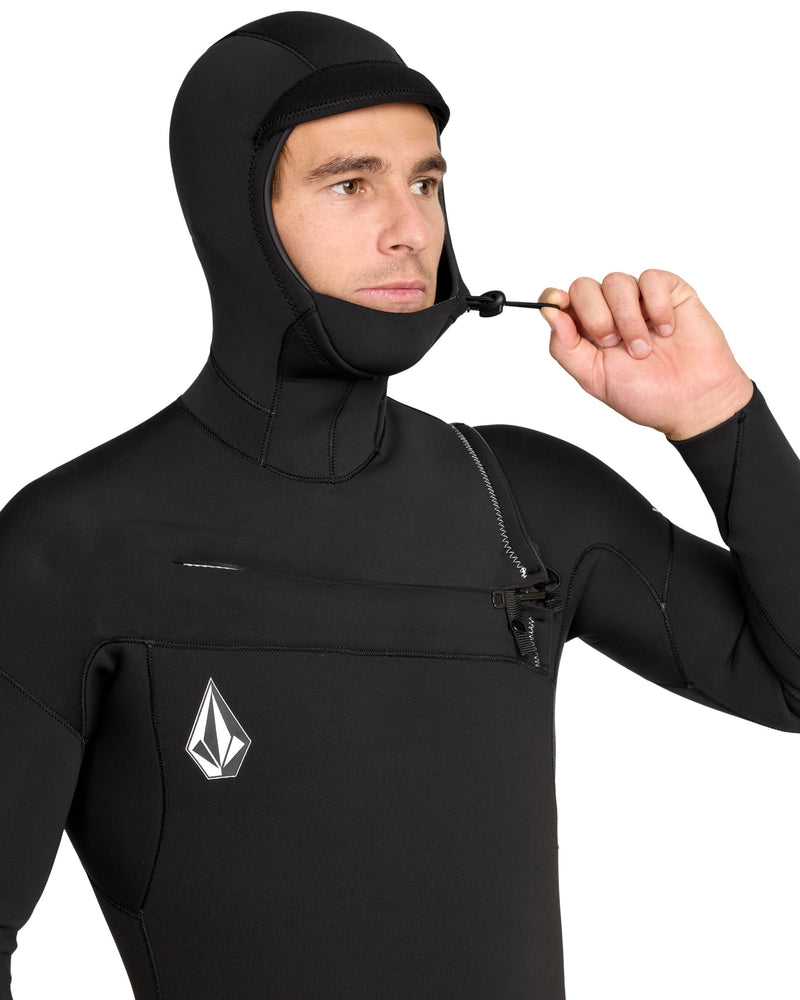 A person adjusts the hood’s drawstring on the Volcom Men's 4/3MM Hooded Chest Zip Full Wetsuit, which features a white geometric logo, shoulder chest zip, and limestone-based neoprene.