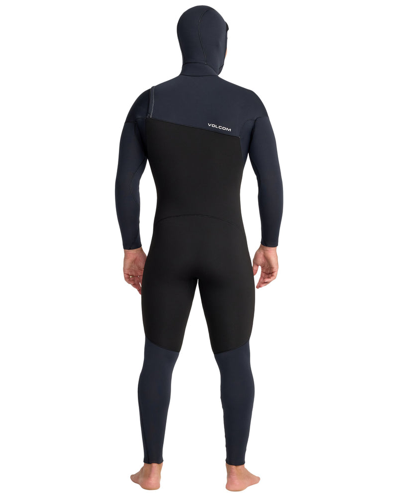 A person stands barefoot against a white background, viewed from the back, wearing the Volcom Men's 5/4/3 Modulator Hooded Chest Zip Full Wetsuit in black and dark blue.