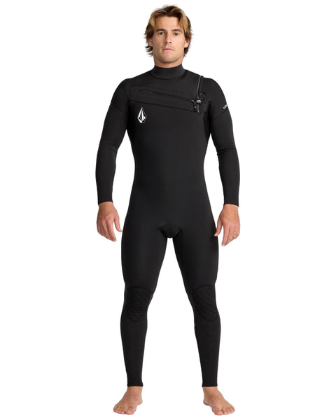 A man stands barefoot facing forward in the Volcom Men's 3/2 Modulator Chest Zip Full Wetsuit, featuring chest zipper and logo details on the chest and sleeve, against a plain white background.