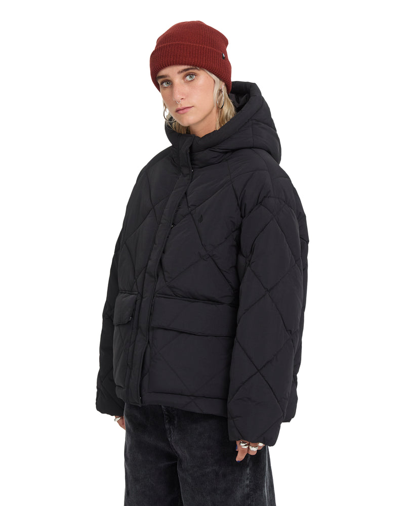 A person wearing a black quilted Volcom Women’s Out Of Boxy Puff and a maroon beanie.