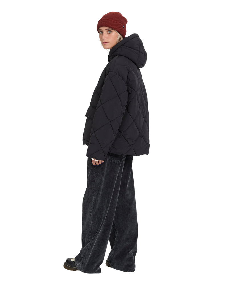 A person wearing a black Volcom Women’s Out Of Boxy Puff quilted heavyweight puffer jacket with a hood, a maroon beanie, and wide-leg black jeans.