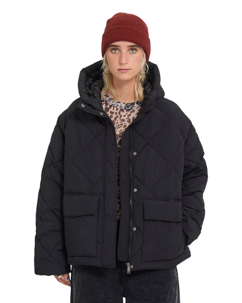 A person wearing a black quilted Volcom Women’s Out Of Boxy Puff cropped jacket with a hood and two front flap pockets.