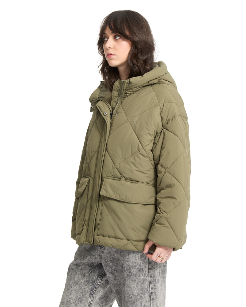 A person wearing an olive green, diamond-quilted Volcom Out Of Boxy Puff heavyweight puffer jacket with an adjustable hood and large front pockets.
