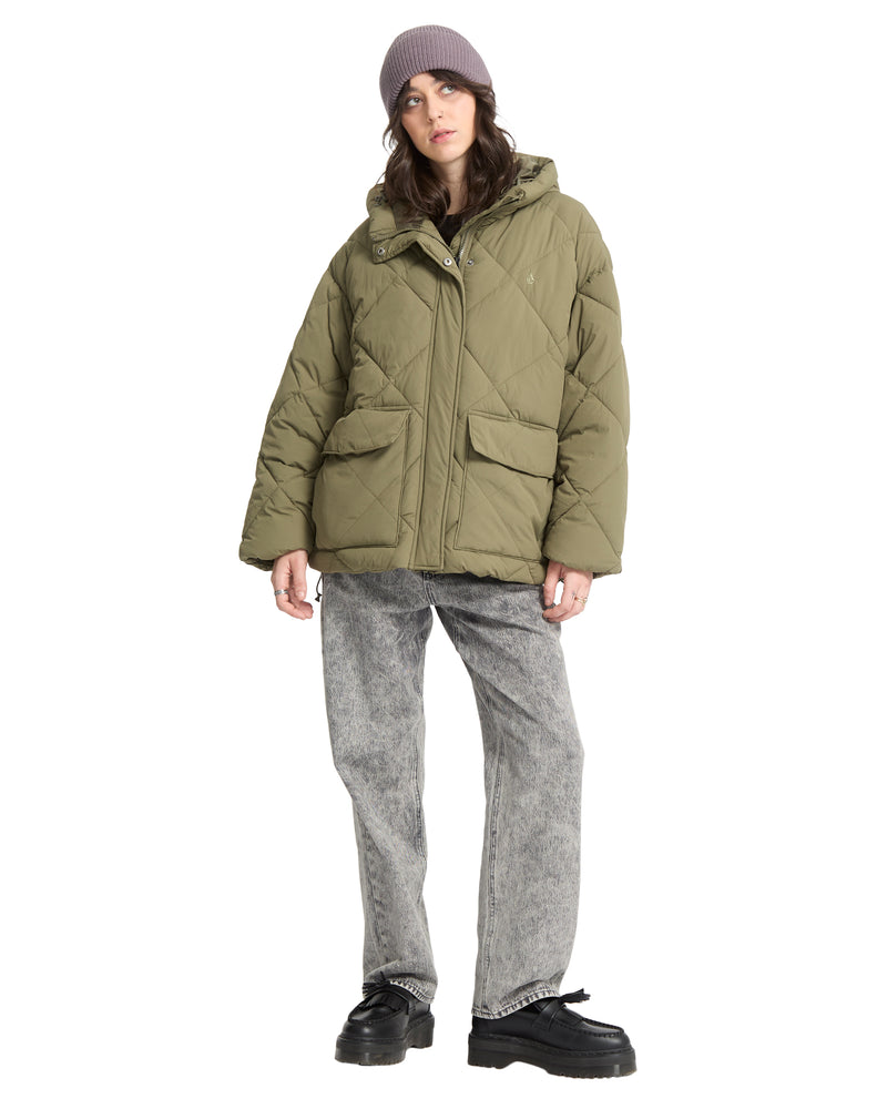 A person wearing a Volcom Out Of Boxy Puff olive green cropped puffer jacket with an adjustable hood, grey jeans, and black loafers.