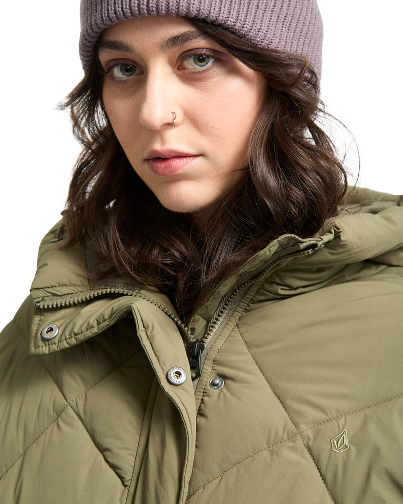 A person wearing a mauve knit beanie and an olive green Volcom Out Of Boxy Puff cropped puffer with an adjustable hood.