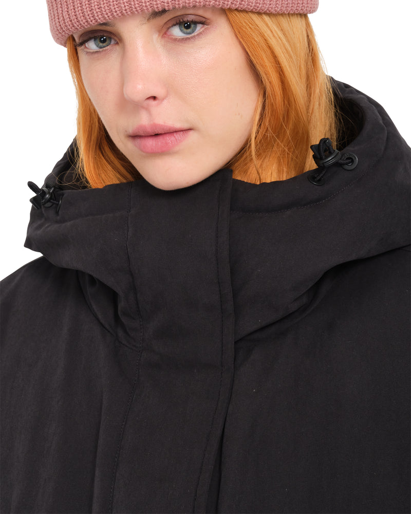 A person wearing a Volcom Women’s Sleepi Puff Up Parka in black with a pink beanie.