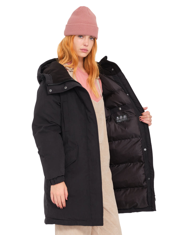 A woman wears a pink beanie and an open Volcom Women’s Sleepi Puff Up Parka, revealing the quilted interior lining of the relaxed fit, heavyweight puffer.