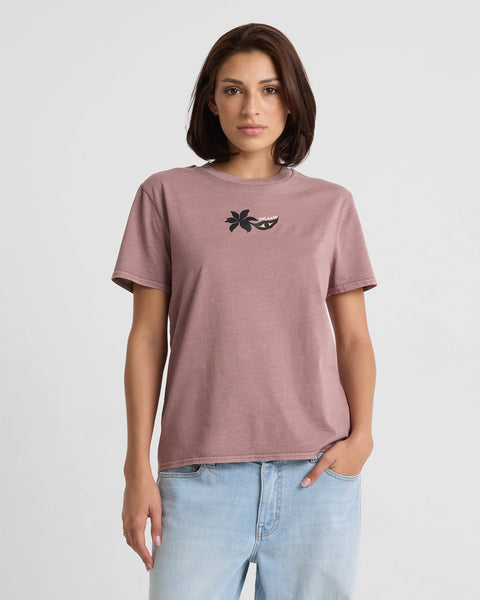 A woman with straight brown hair wears the Volcom Women’s Lock It Up Short Sleeve Tee in Star White, featuring a small black palm tree and smiling mouth graphic, paired with light blue jeans against a plain white background.