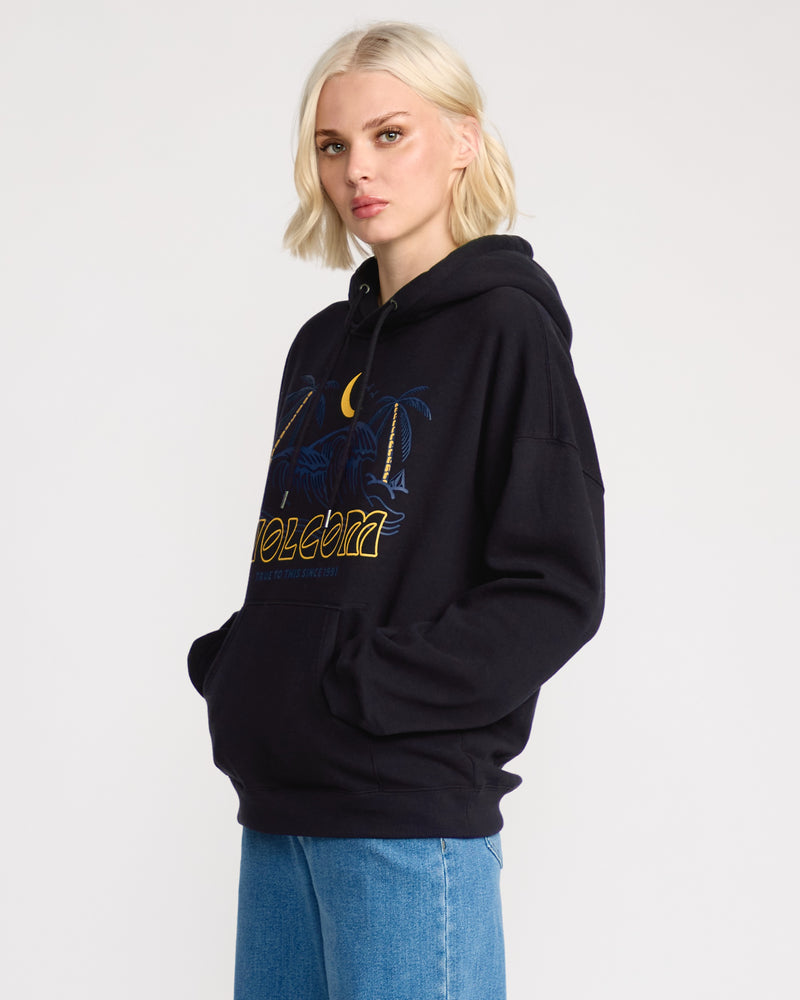 A woman with short blonde hair wears the Volcom Women's Stone Art Up Hoodie in a dropped-shoulder fit with a colorful graphic, paired with blue jeans. She stands hands-in-pockets against a plain light background.