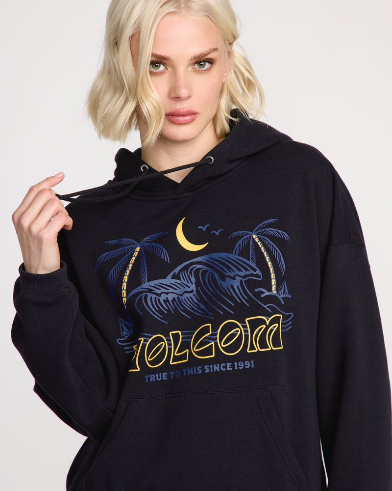 A woman with short blonde hair wears the Volcom Women's Stone Art Up Hoodie, showcasing a dropped-shoulder fit with palm trees, waves, a crescent moon, birds, and “Volcom True to This Since 1991” text.
