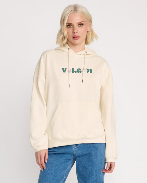 A woman with short blonde hair models the Volcom Women's Stone Art Up Hoodie, a cream-colored oversized style with green and pink VOLCOM logo, paired with blue jeans against a white background—ideal for relaxed streetwear looks.