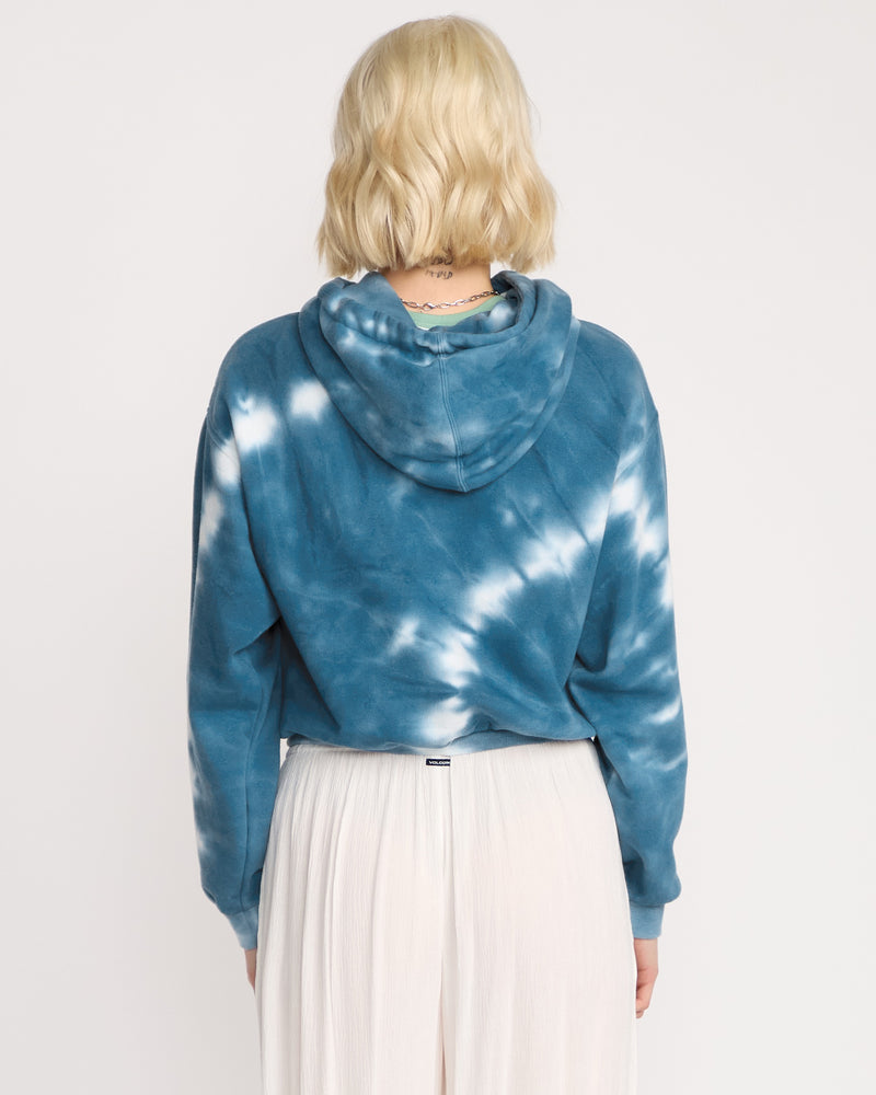 A woman with short blonde hair, seen from behind, wears the Volcom Women's New Tie Dye Hoodie in blue and white paired with a long white pleated skirt, standing against a plain white background.