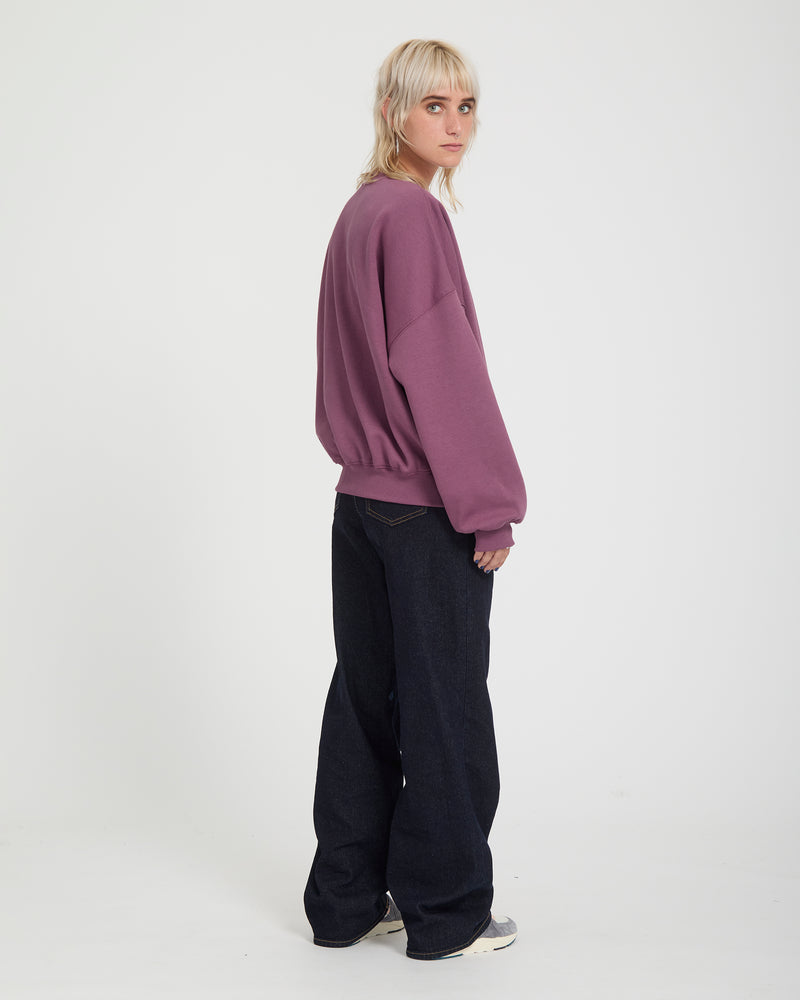 A person wears a plum-colored, heavyweight, oversized Volcom Sto N Crew sweatshirt with dark wide-leg jeans.